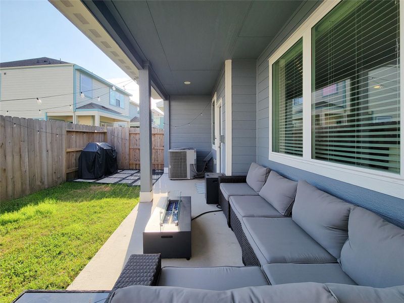 Covered patio with comfortable seating, a modern outdoor table, and a view of a small fenced backyard. It features a grill area and is ideal for relaxation and entertaining.