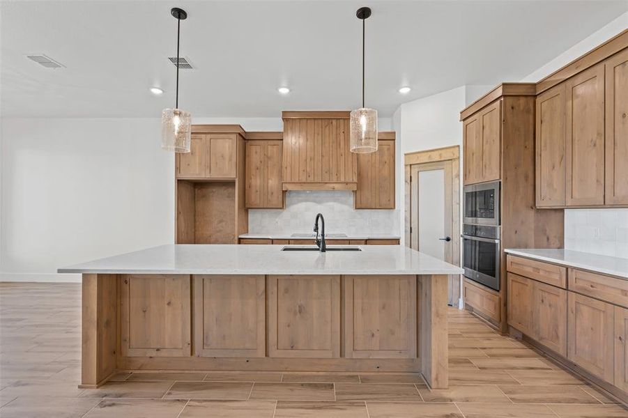 Kitchen featuring light stone counters, hanging light fixtures, wood finish floors, decorative backsplash, and recessed lighting