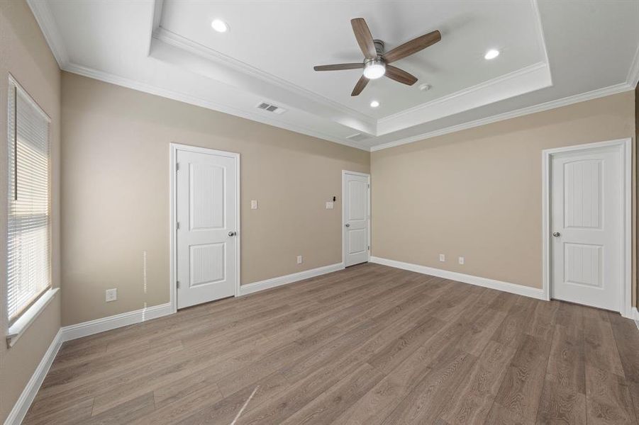 Unfurnished bedroom featuring light wood-style floors, visible vents, and a raised ceiling