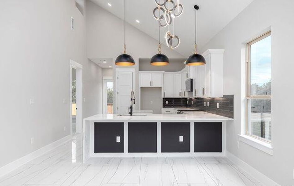 Modern kitchen featuring a large island with white countertops and dark paneling, a dark tiled backsplash, white cabinetry, and stainless steel appliances