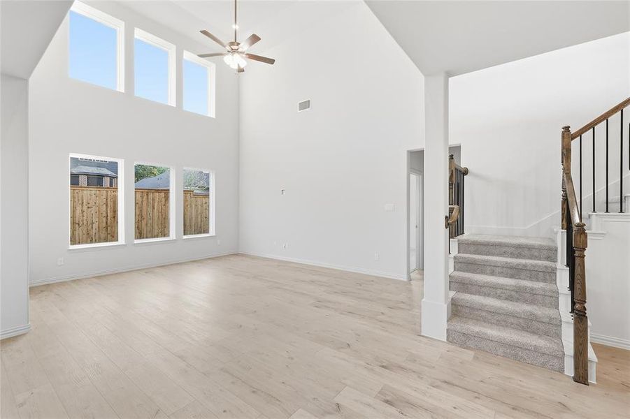 Unfurnished living room featuring stairs, a high ceiling, ceiling fan, and light wood-style floors