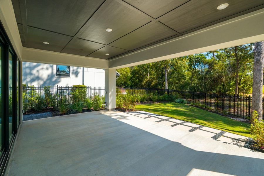 This photo showcases a spacious, covered patio with a modern design, overlooking a well-maintained, fenced backyard with lush greenery and mature trees, perfect for outdoor relaxation and entertaining.