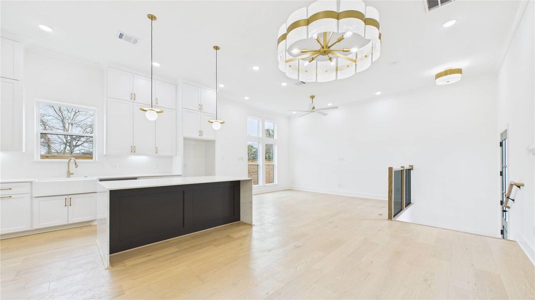 This open-concept living space features a modern kitchen with sleek white cabinetry, a large island, and elegant gold-accented lighting. The room is bright and airy with high ceilings, natural light, and hardwood floors, offering a seamless flow into the living area.