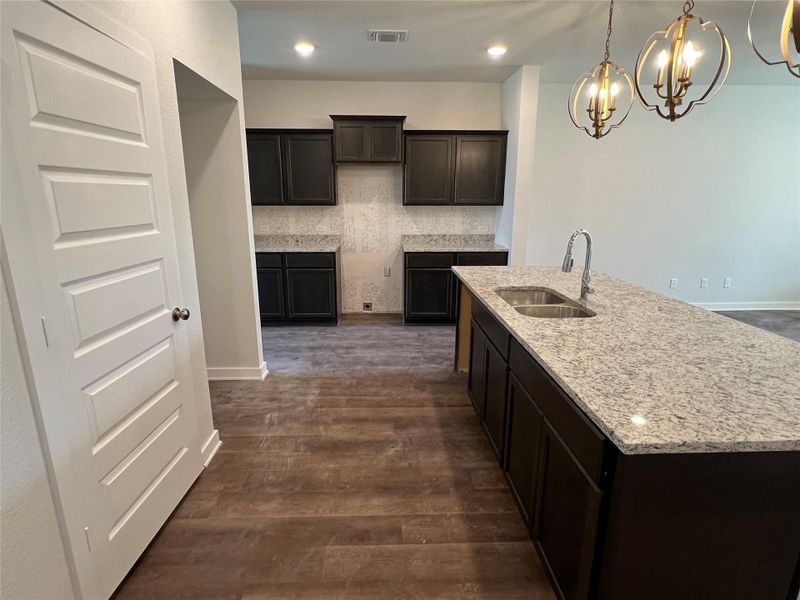 Kitchen with light stone countertops, dark brown cabinetry, dark wood-style floors, a chandelier, and recessed lighting Kitchen with light stone countertops, dark brown cabinetry, dark wood-style floors, a chandelier, and recessed lighting