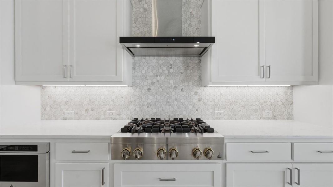 Kitchen with wall chimney exhaust hood, white cabinets, appliances with stainless steel finishes, light stone counters, and decorative backsplash Kitchen with wall chimney exhaust hood, white cabinets, appliances with stainless steel finishes, light stone counters, and decorative backsplash