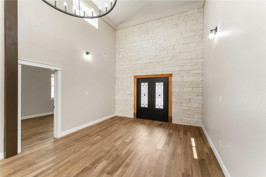 This room features high ceilings and a statement stone accent wall with elegant metal rod iron double doors. The tile floors and large chandelier add warmth and sophistication, while ample natural light enhances the spaciousness.