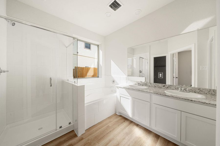 This elegant primary bath features a soaking tub, separate glass-enclosed shower, and dual vanities with ample counter space. Soft natural light and modern finishes create a clean, refreshing atmosphere. This elegant primary bath features a soaking tub, separate glass-enclosed shower, and dual vanities with ample counter space. Soft natural light and modern finishes create a clean, refreshing atmosphere.