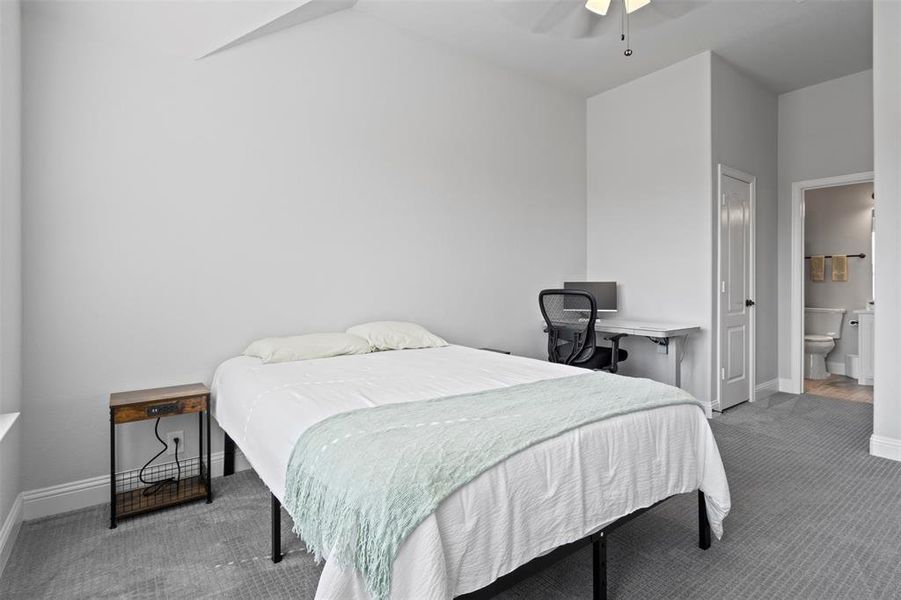 Carpeted bedroom featuring ceiling fan, vaulted ceiling, and ensuite bath