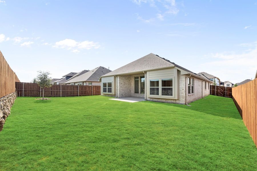 Brick home rear exterior with large green backyard, small patio, and wood privacy fence Brick home rear exterior with large green backyard, small patio, and wood privacy fence