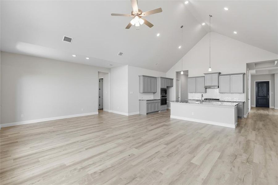 Unfurnished living room with a high ceiling, a ceiling fan, light wood-style floors, and recessed lighting