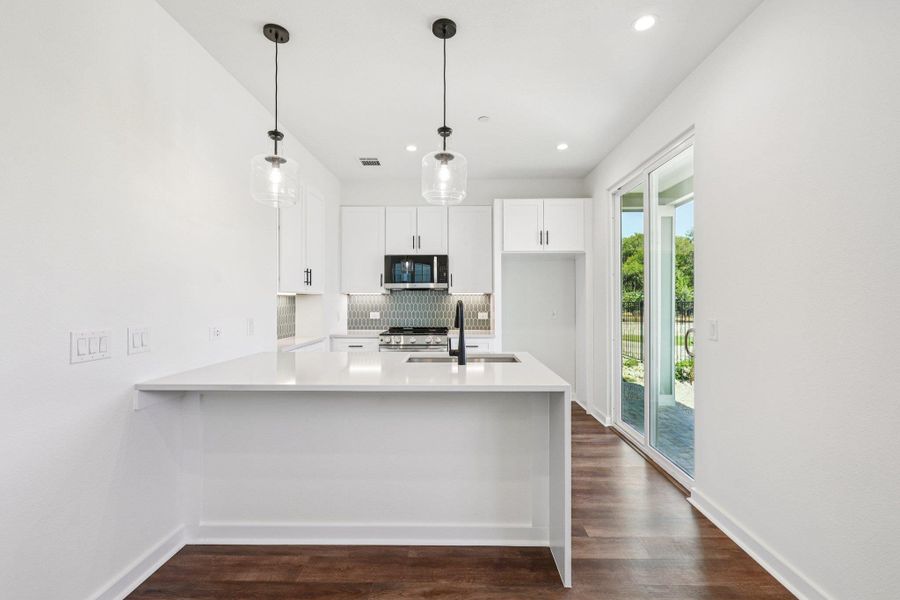 Kitchen featuring decorative backsplash, a peninsula, white cabinets, dark wood-type flooring, and recessed lighting Kitchen featuring decorative backsplash, a peninsula, white cabinets, dark wood-type flooring, and recessed lighting
