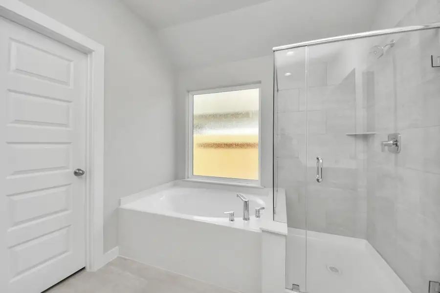 Escape to a spa-like oasis in this primary bathroom. Enjoy a walk-in shower with tile surround, a separate garden tub with custom detailing, and an elegant vanity featuring light countertops, modern hardware, and beautiful recessed lights. Experience luxury and relaxation in every detail. Sample photo of completed home with similar floor plan. Actual colors and selections may vary.