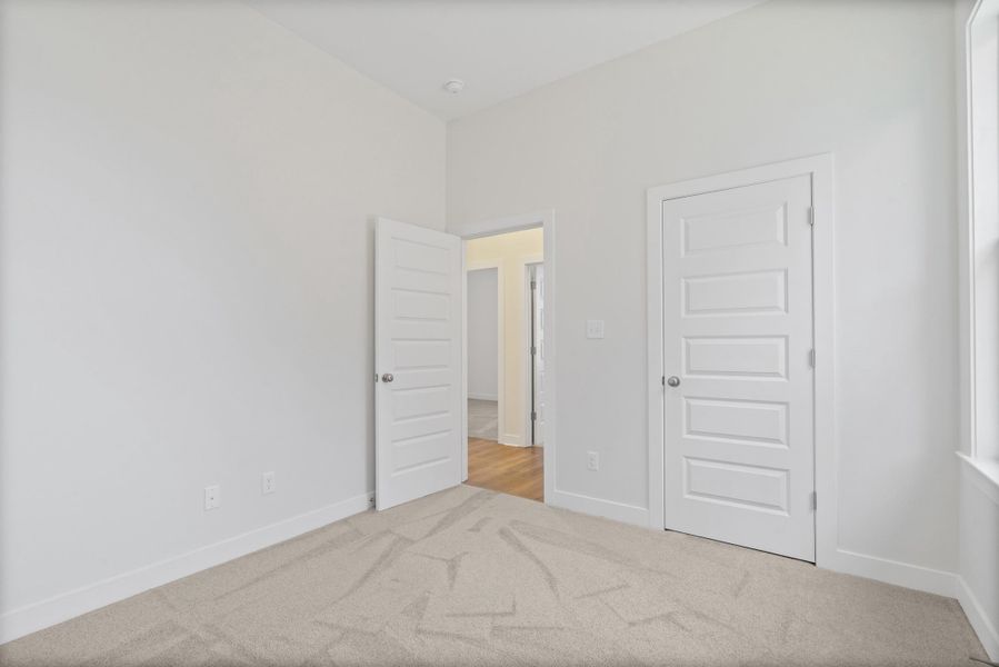 Unfurnished bedroom with light carpet and baseboards