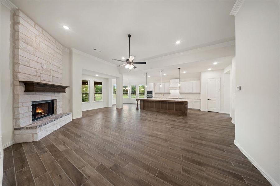 Unfurnished living room with ornamental molding, a ceiling fan, a fireplace, recessed lighting, and dark wood-style flooring