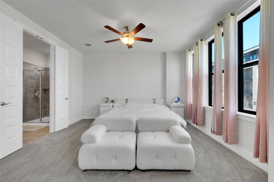 Bedroom featuring ceiling fan, light carpet, and ensuite bath