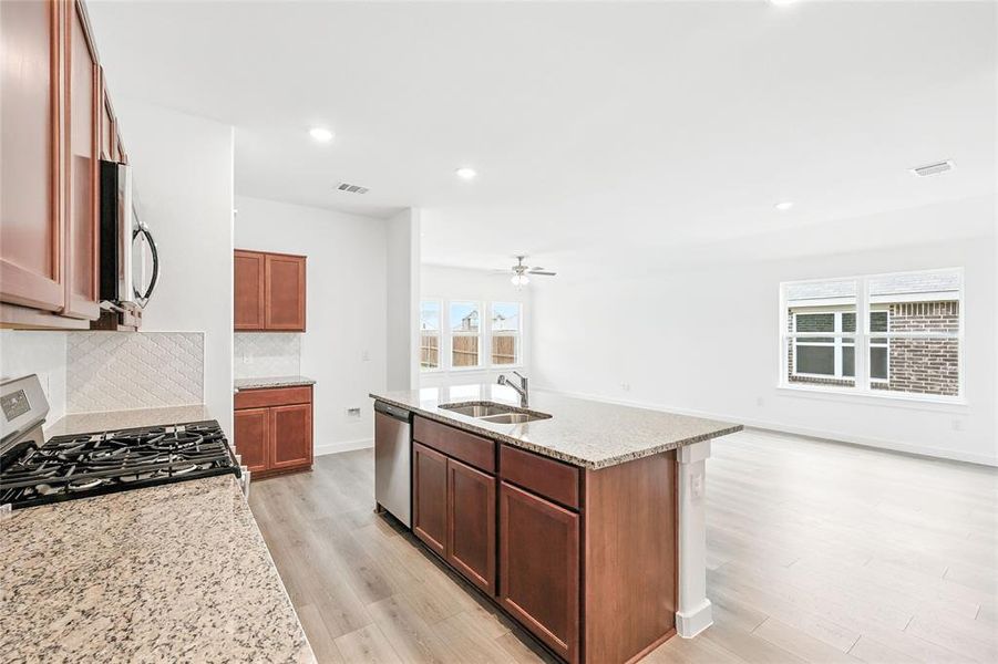 Kitchen with light stone countertops, recessed lighting, tasteful backsplash, light wood-type flooring, and a kitchen island with sink Kitchen with light stone countertops, recessed lighting, tasteful backsplash, light wood-type flooring, and a kitchen island with sink