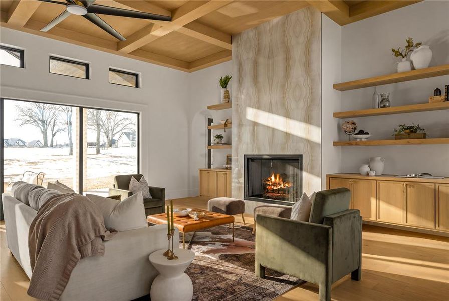 Living area featuring a stone-clad fireplace, coffered wood-finish ceiling, large sliding glass doors, built-in open shelving, and light wood-finish flooring