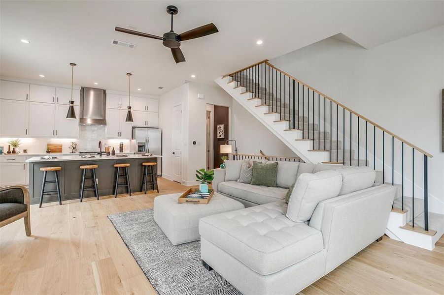 Living area with stairway, light wood-style flooring, ceiling fan, and recessed lighting Living area with stairway, light wood-style flooring, ceiling fan, and recessed lighting