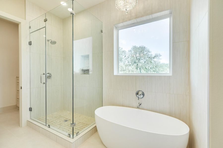 This bathroom features a modern glass-enclosed shower and a sleek freestanding tub. Natural light pours in through a large window, highlighting the elegant tile work and creating a serene, spa-like atmosphere.