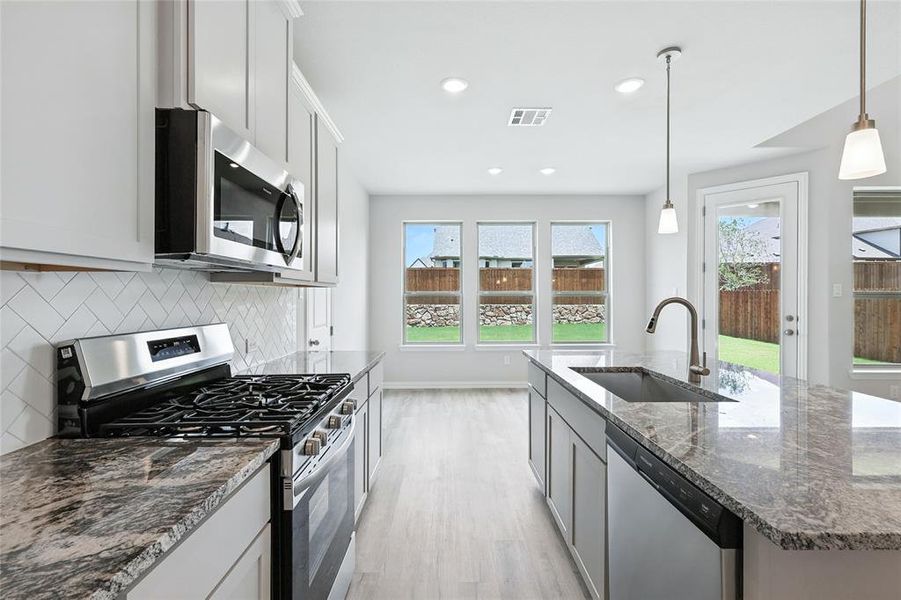 Kitchen featuring stainless steel appliances, backsplash, light wood-type flooring, dark stone counters, and a kitchen island with sink Kitchen featuring stainless steel appliances, backsplash, light wood-type flooring, dark stone counters, and a kitchen island with sink