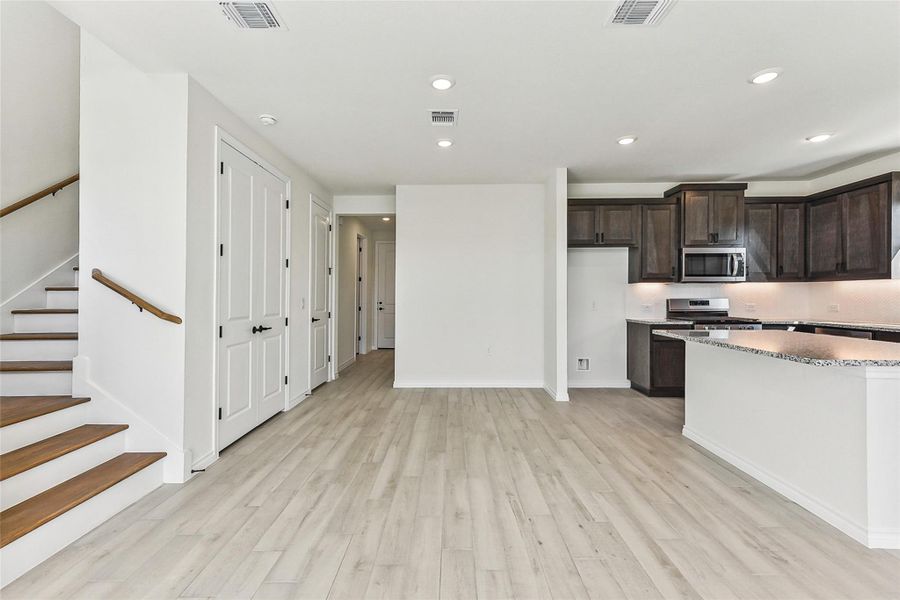 Kitchen with light wood-type flooring, dark brown cabinets, visible vents, and stainless steel appliances Kitchen with light wood-type flooring, dark brown cabinets, visible vents, and stainless steel appliances