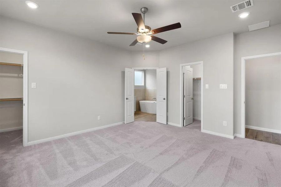 A spacious primary bedroom features soft carpeting, a ceiling fan, and convenient access to a private bath and walk-in closet.