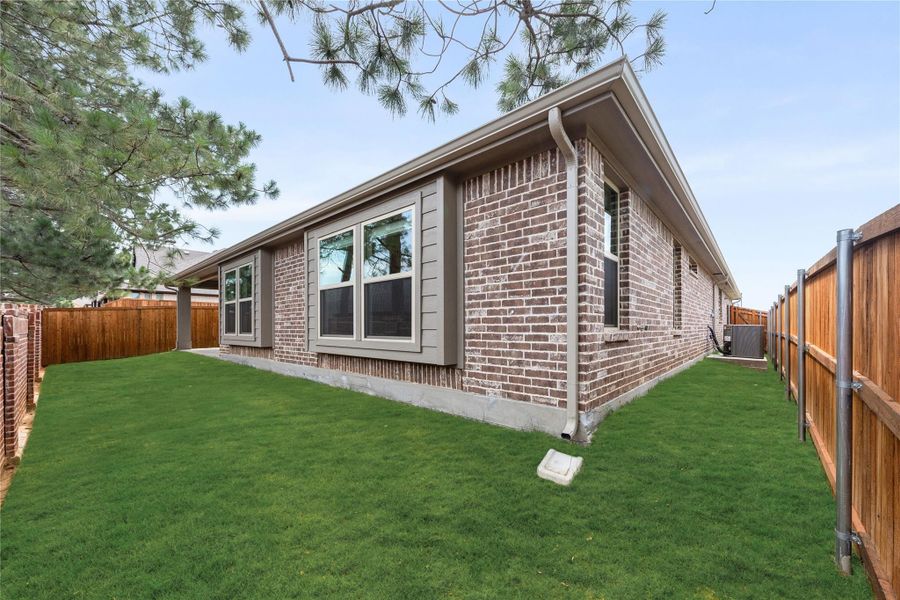 Brick home exterior with large windows, green backyard lawn, and wood privacy fence