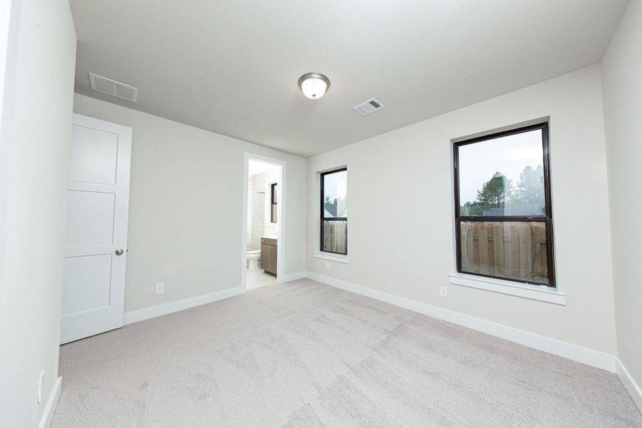 The ideal setup for multi-generational living or extended stays, this guest bedroom on the first floor includes its own dedicated en suite bath. It features high ceilings, large windows, plush carpet flooring, and neutral-toned walls.
