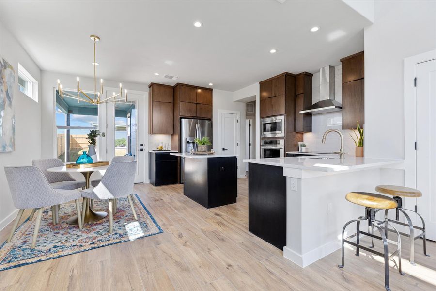 Kitchen with a breakfast bar, a chandelier, a center island, wall chimney range hood, and light wood-style flooring