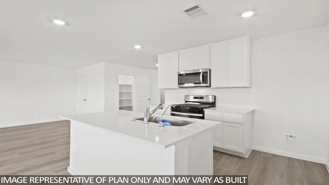 Open-concept kitchen featuring a central island with an undermount sink, white cabinetry, integrated stainless steel appliances, and wood-finish flooring
