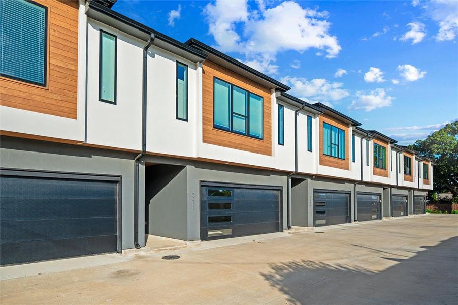 Front Exterior features matching stucco and cedar accents throughout the townhome row. Black-framed windows complement the modern design. Individual garages and private entries line the front elevation.