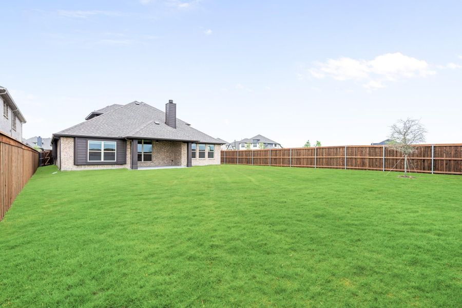 Large backyard with green lawn, wood privacy fence, and brick home with chimney visible in background