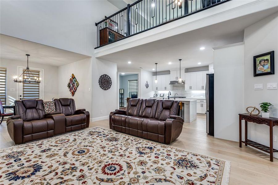 Living area featuring light wood-style flooring, hanging lights, and a high ceiling