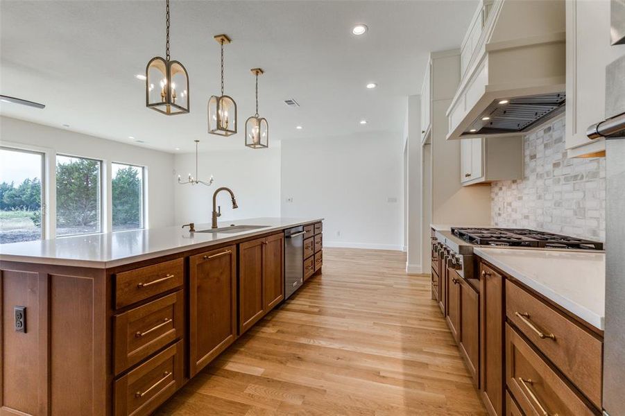 Kitchen with a chandelier, a sink, stainless steel appliances, tasteful backsplash, and a center island with sink
