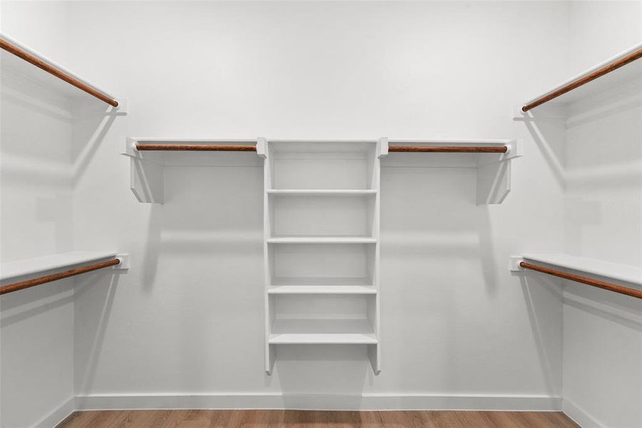 Walk-in closet featuring white built-in shelving, multiple hanging rods, and wood-finish flooring Walk-in closet featuring white built-in shelving, multiple hanging rods, and wood-finish flooring