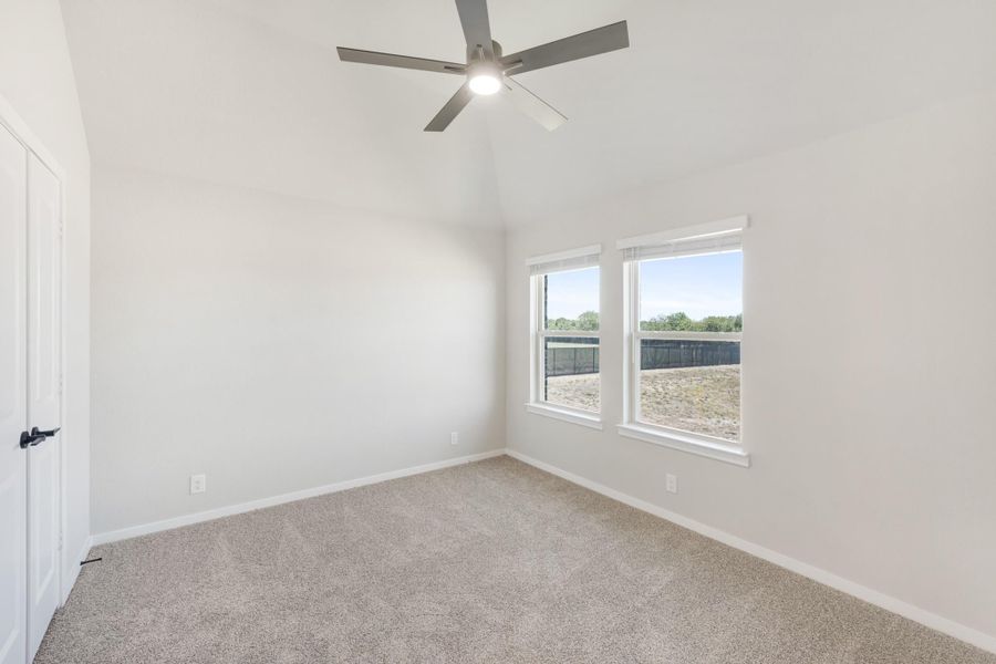 Empty bedroom with vaulted ceiling, ceiling fan, carpet flooring, and two windows with backyard view