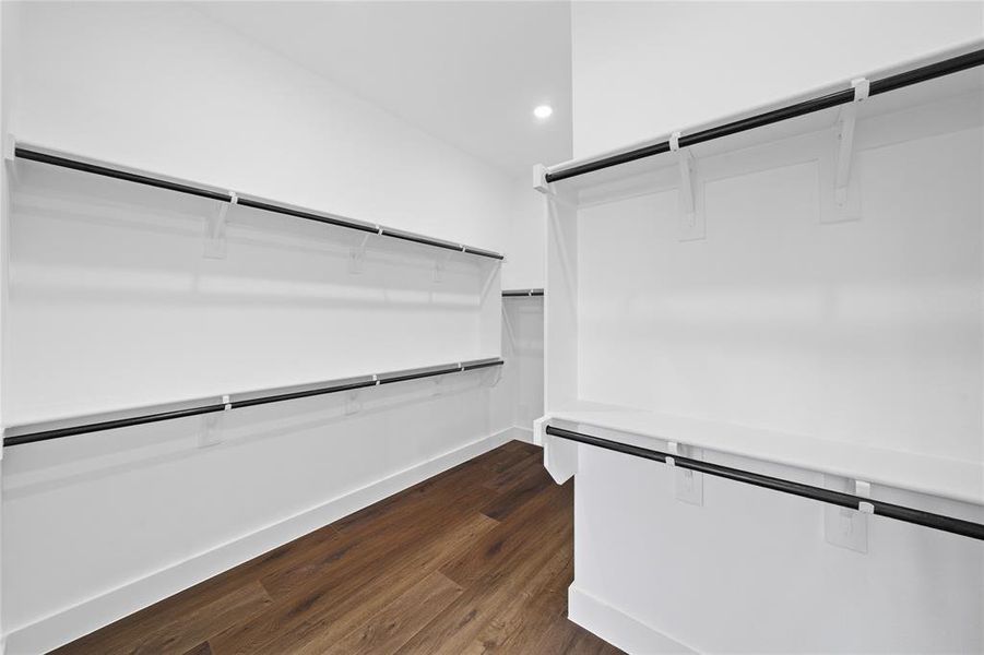 Spacious closet featuring multiple white shelving units, black hanging rods, and wood-finish flooring