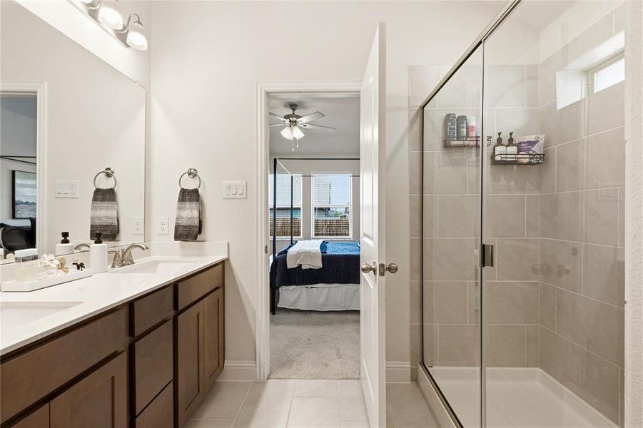 Bathroom featuring a dual vanity with a light-colored countertop and wood-finish cabinetry, a large mirror, and a frameless glass shower enclosure with tiled walls and a small transom window