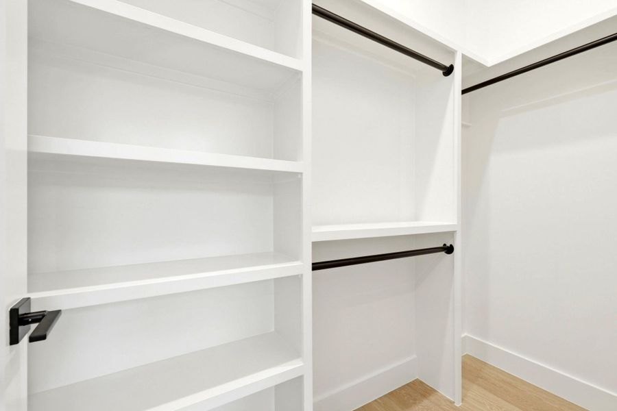 Built-in closet system featuring white shelving, multiple hanging rods, and light wood-finish flooring