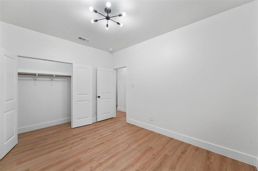 Spacious interior room featuring wood-finish flooring, white walls, and a contemporary ceiling light fixture Spacious interior room featuring wood-finish flooring, white walls, and a contemporary ceiling light fixture