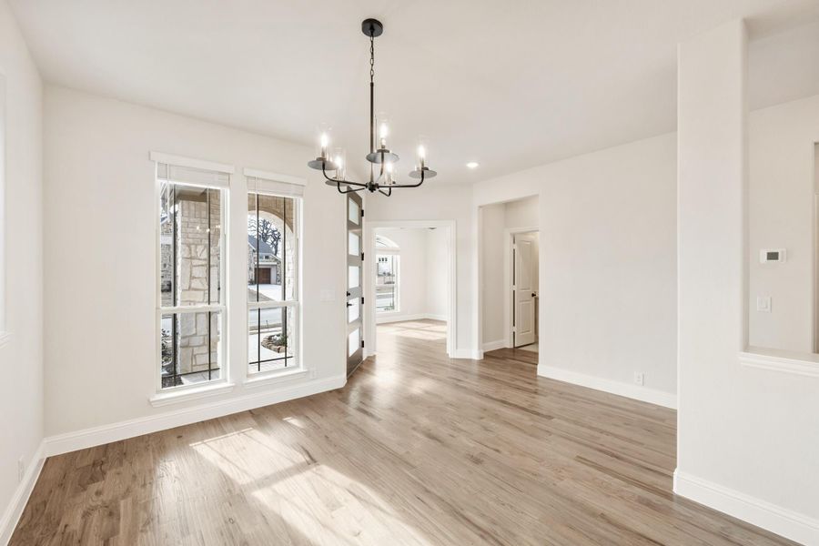 Empty dining room with light hardwood floors, black chandelier, and large windows with natural light