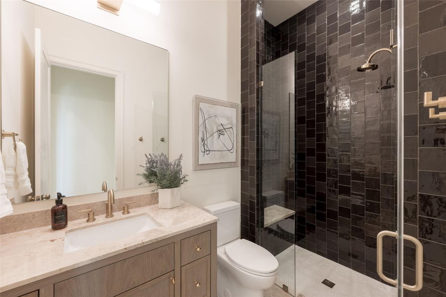This guest bathroom balances bold and organic with handmade espresso-toned shower tile and a softly veined cappuccino marble countertop. Brass plumbing fixtures and natural wood cabinetry add warmth, while the full bath layout makes it ideal for use as a guest suite or multi-generational space. This guest bathroom balances bold and organic with handmade espresso-toned shower tile and a softly veined cappuccino marble countertop. Brass plumbing fixtures and natural wood cabinetry add warmth, while the full bath layout makes it ideal for use as a guest suite or multi-generational space.