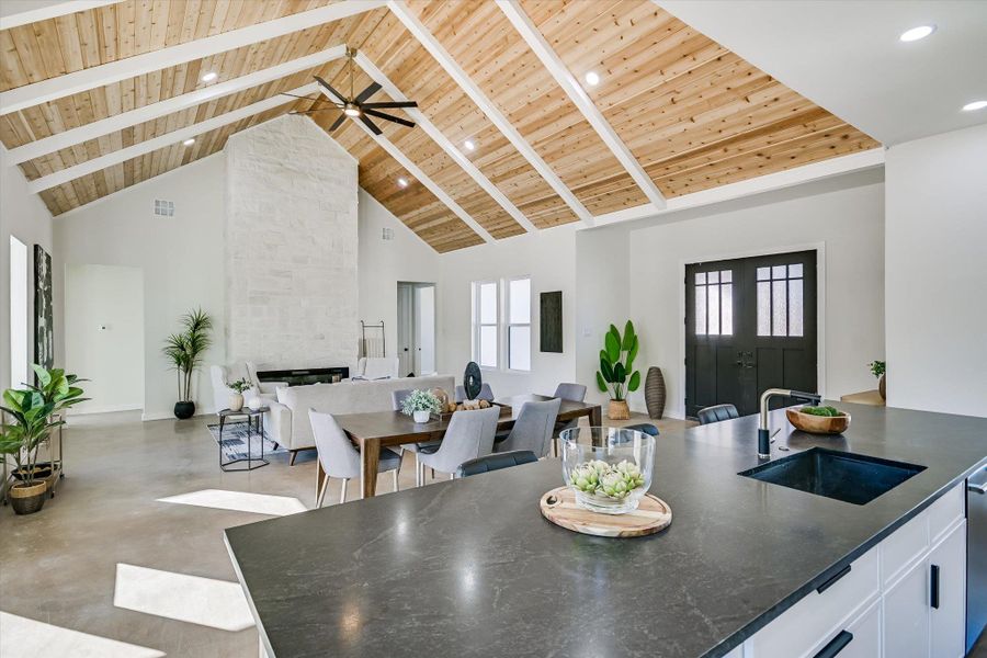 Dining room with a wood ceiling with exposed beams, high vaulted ceiling, finished concrete flooring, a fireplace, and a ceiling fan