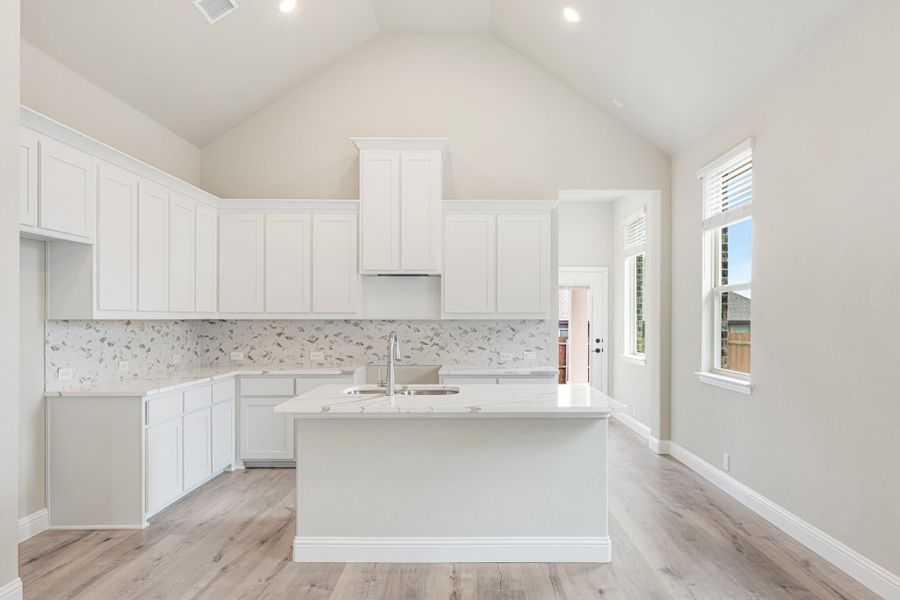 White kitchen with vaulted ceiling, center island with sink, white cabinets, and light wood floors