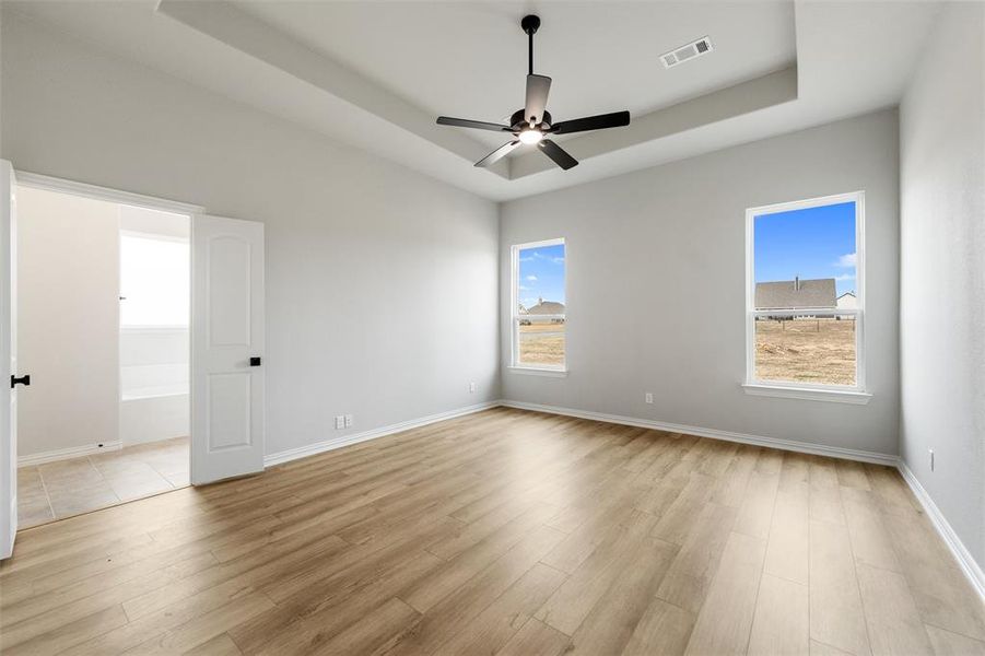 Spare room featuring a raised ceiling, light wood-type flooring, and ceiling fan Spare room featuring a raised ceiling, light wood-type flooring, and ceiling fan