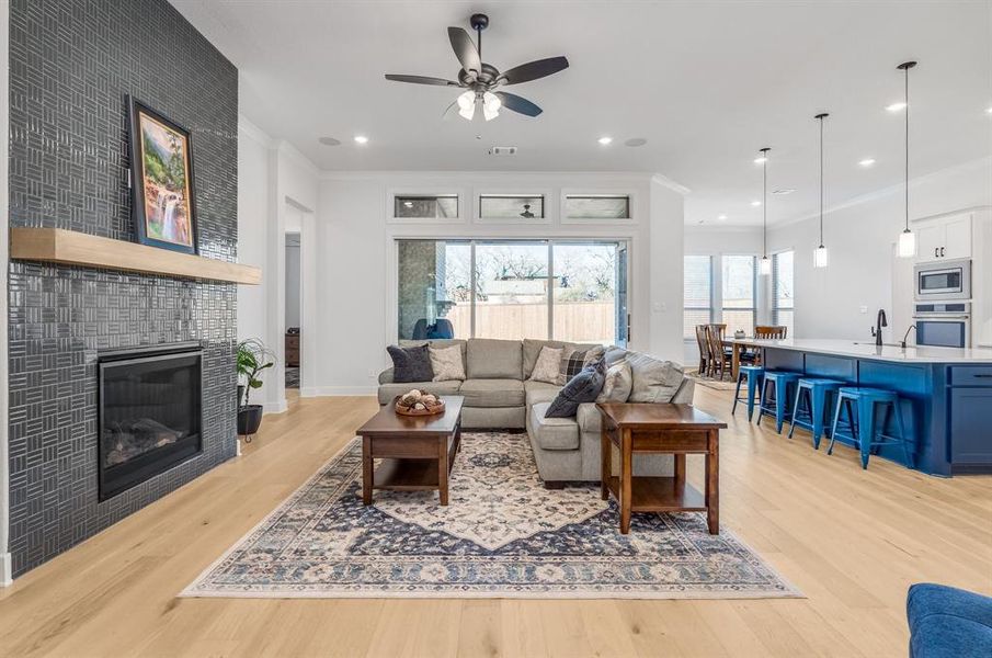 Living room with ceiling fan, ornamental molding, a tile fireplace, and light hardwood / wood-style flooring