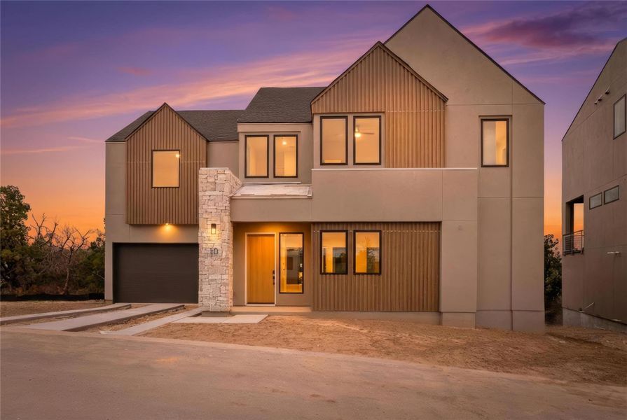 View of front of home with driveway, an attached garage, stone siding, and stucco siding