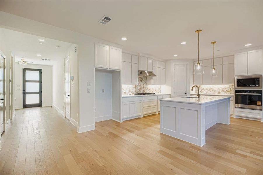 Kitchen featuring white cabinetry, appliances with stainless steel finishes, light wood-style flooring, pendant lighting, and a center island with sink Kitchen featuring white cabinetry, appliances with stainless steel finishes, light wood-style flooring, pendant lighting, and a center island with sink