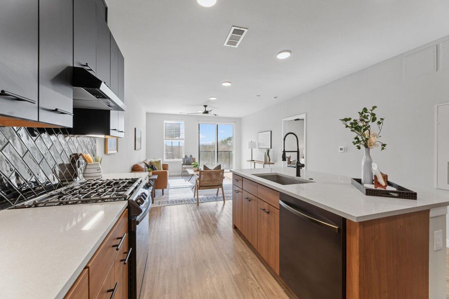 Kitchen featuring stainless steel appliances, light stone countertops, open floor plan, an island with sink, and light wood-style flooring
