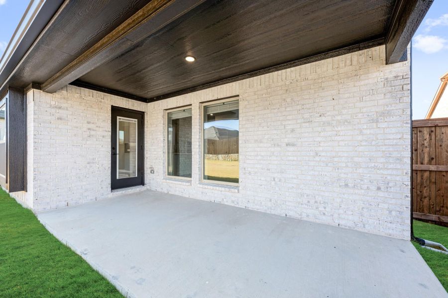 Covered back patio with concrete slab, white brick exterior, dark wood ceiling, and glass door entry Covered back patio with concrete slab, white brick exterior, dark wood ceiling, and glass door entry